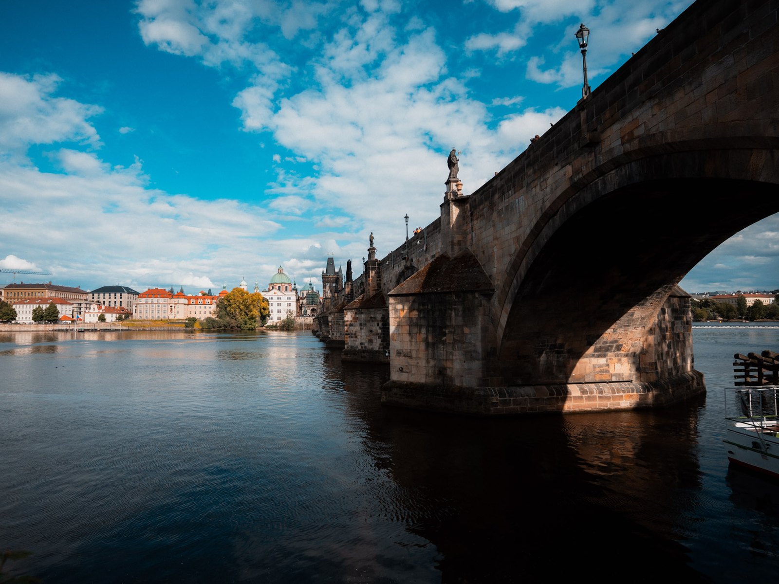 Karlův most z boku od Kampy, vidět oblouky, pilíře a staroměstské domy za řekou